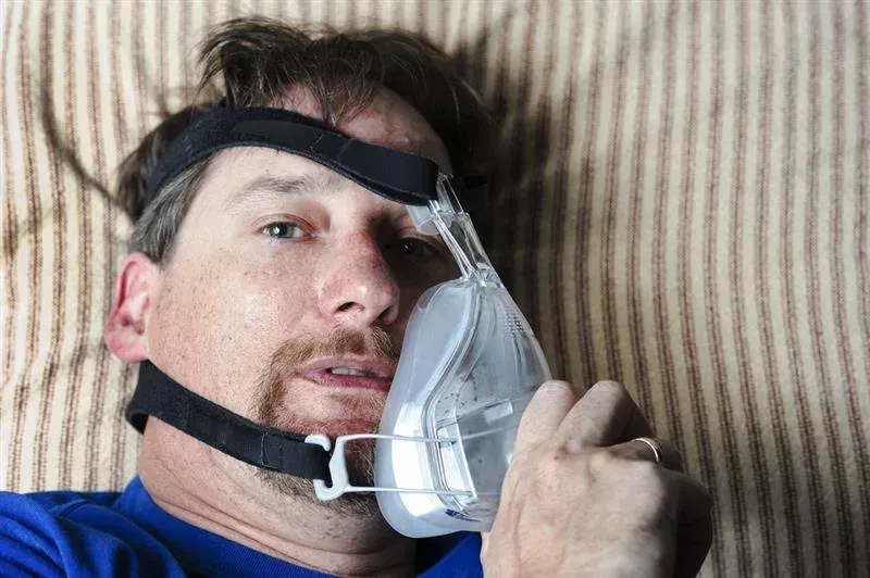 man lying down taking off his CPAP mask, uncomfortable